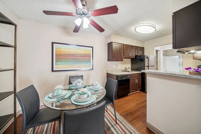 Chic dining area with modern round glass table, elegant place settings, stylish kitchen with dark cabinetry, and inviting open space.