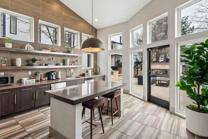 Modern kitchen with high ceilings, sleek open shelving, large windows, and an elegant island with bar seating.
