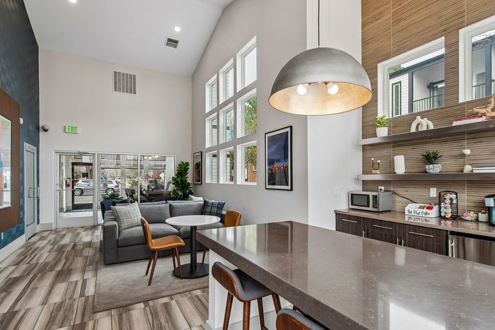 Modern, sunlit communal lounge with vaulted ceilings, stylish seating area, and a kitchenette with sleek countertops.