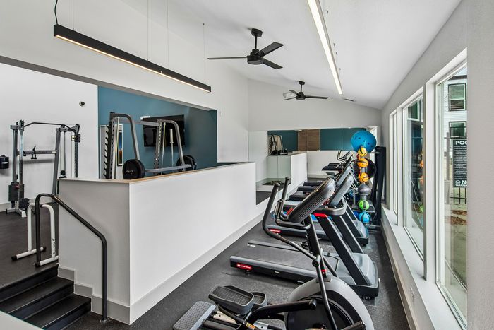 Contemporary fitness center with abundant natural light, featuring modern treadmills, exercise equipment, and vibrant decor.