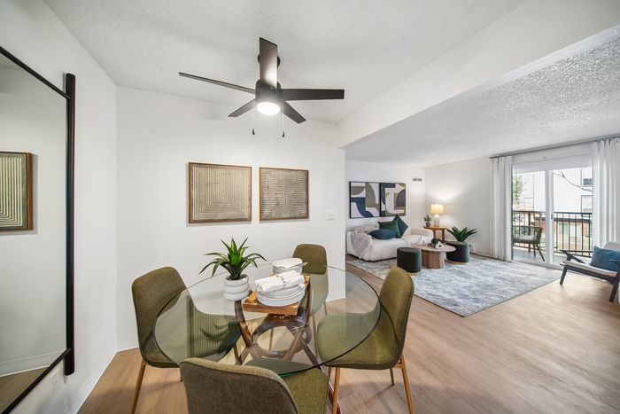 Contemporary open-plan living and dining area featuring a glass dining table with stylish chairs, cozy seating with modern art, and natural light from large sliding doors.