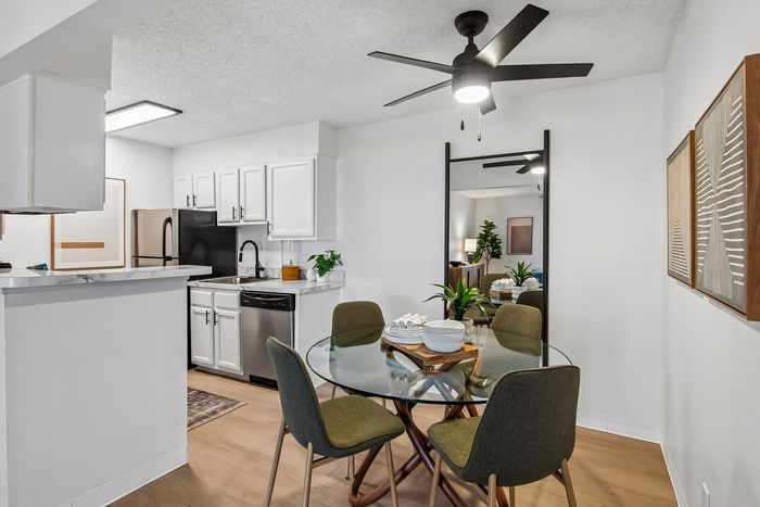 Chic apartment interior showcasing sleek modern kitchen with white cabinetry, accented by a stylish dining area with a glass table and elegant seating.