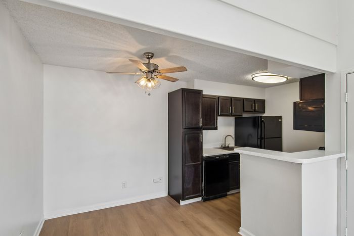 Charming apartment kitchen with sleek dark cabinetry, modern appliances, and elegant ceiling fan, offering a cozy and inviting ambiance.