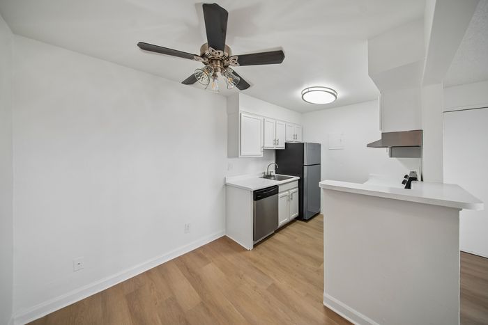 Modern kitchen with sleek stainless steel appliances, elegant white cabinetry, and warm wood flooring, enhanced by a stylish ceiling fan for a chic yet functional space.