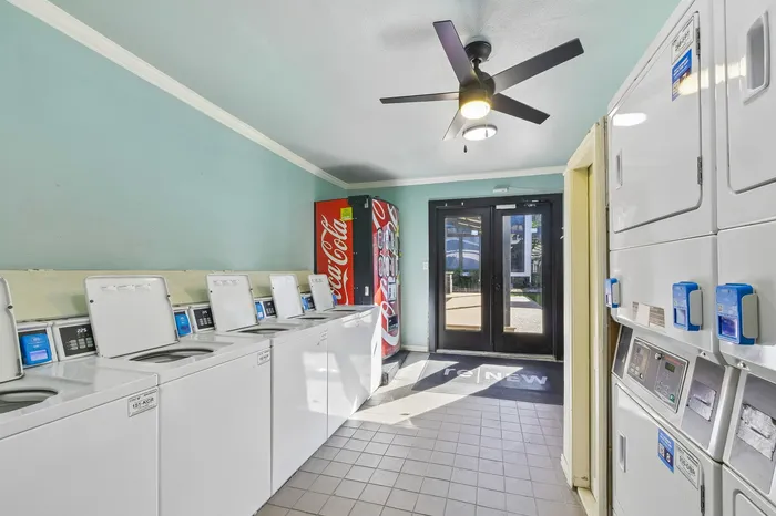 Bright and modern laundry room equipped with multiple washing and drying machines, complete with a convenient vending machine and sleek ceiling fan.