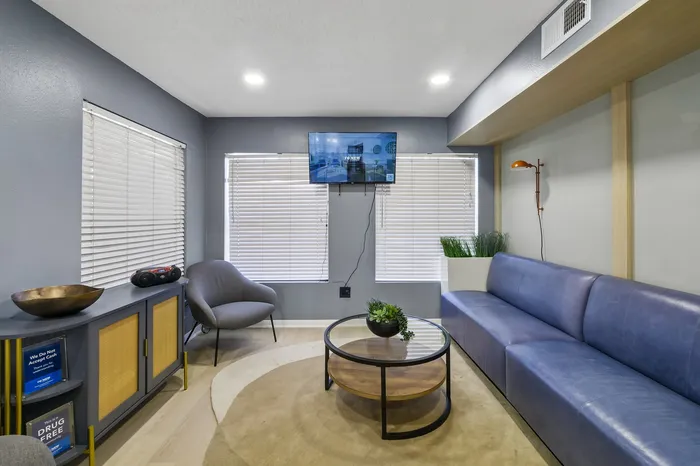 Inviting living space featuring a sleek blue couch, modern armchair, glass coffee table, and mounted TV, perfect for relaxation and entertainment.