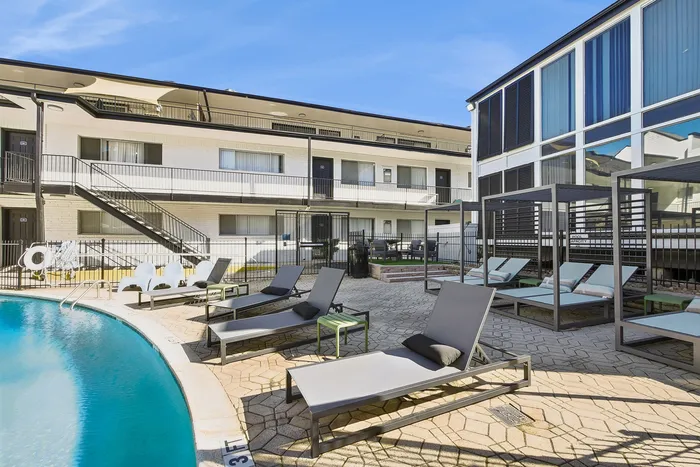 Inviting poolside oasis with modern lounge chairs and stylish cabanas at a sleek apartment complex under clear blue skies.
