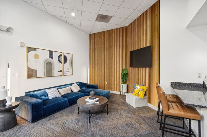 Chic living area with a plush blue velvet sofa, modern art, and a stylish wood accent wall, perfect for relaxation and entertaining.