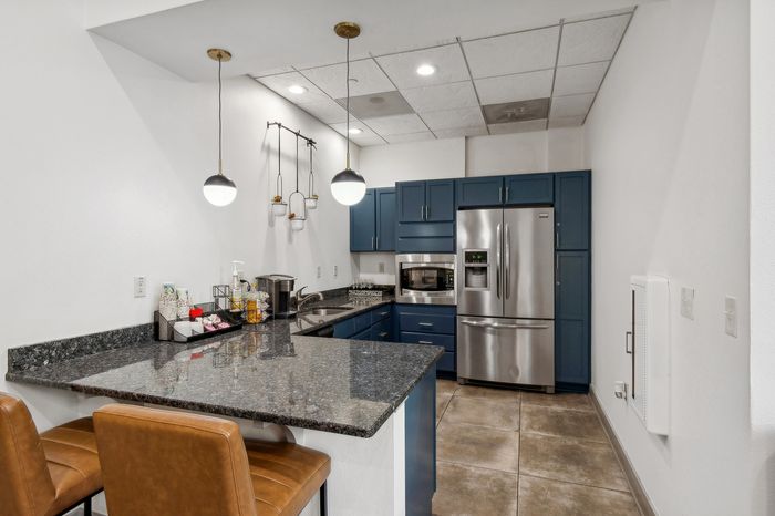 Modern kitchen with elegant blue cabinets, granite countertops, and stainless steel appliances, featuring stylish pendant lighting and cozy seating.