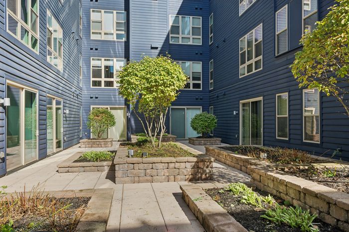Charming apartment courtyard with lush greenery, modern blue siding, and inviting walkways.