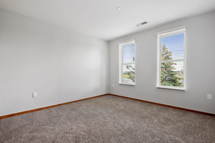 Bright, airy room featuring plush carpet flooring and large windows with serene neighborhood views.