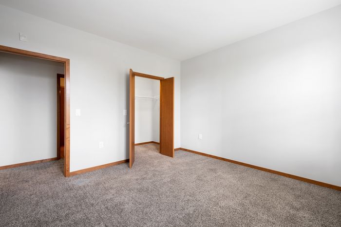 Bright and spacious room with soft carpet flooring, featuring a built-in closet and fresh white walls.