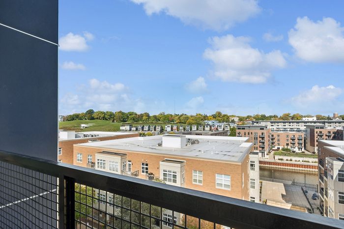 Charming urban balcony view overlooking modern apartment buildings and lush green landscape under a clear blue sky.