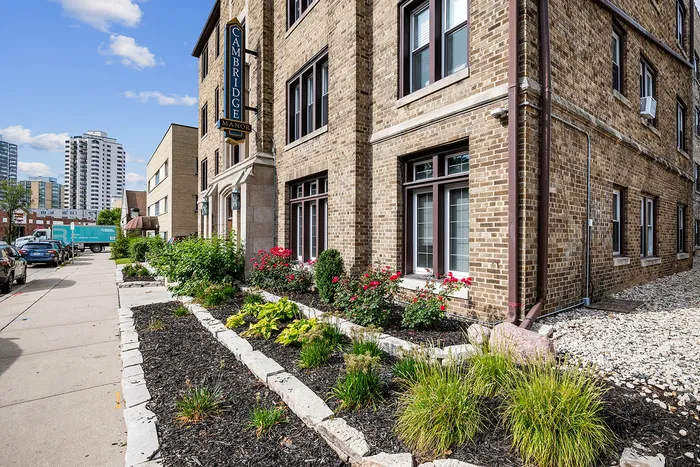 Charming urban apartment building showcasing classic brick architecture, accentuated by vibrant landscaping and flower beds, set against a backdrop of a bustling city street.