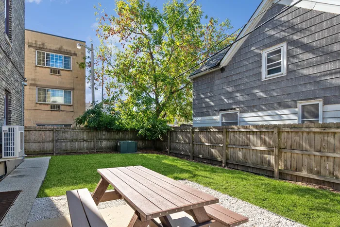 Charming backyard with a picnic table, lush green lawn, surrounded by a rustic wooden fence and shaded by a large tree.
