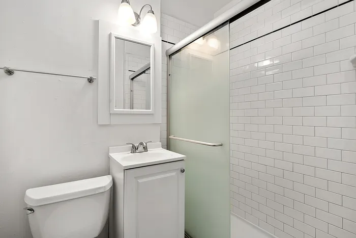 Modern bathroom featuring sleek white tiles, a polished vanity with mirror, and an elegant glass-enclosed shower.