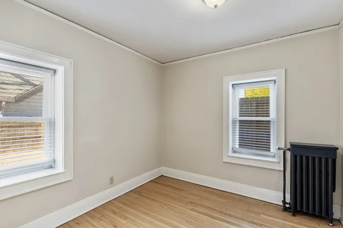 Bright and inviting room with abundant natural light from dual windows, featuring elegant light hardwood floors and a classic radiator.