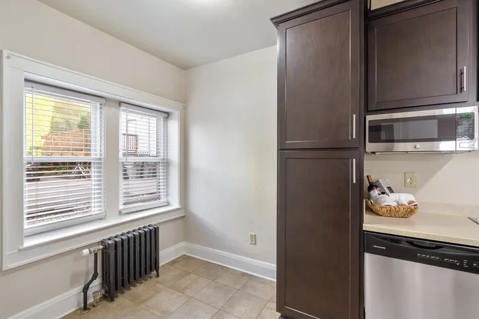 Bright kitchen area with sleek dark wood cabinets, stainless steel appliances, and charming natural light streaming through white-framed windows.