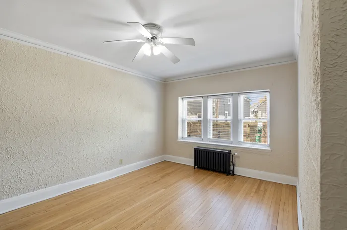 Bright and airy room with elegant ceiling fan, hardwood floors, and large windows inviting natural light.