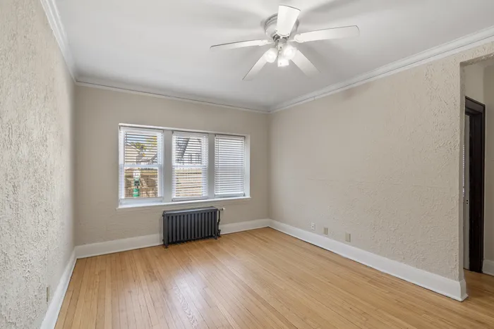 Charming, light-filled room with elegant textured walls, hardwood flooring, and a modern ceiling fan, perfect for cozy living.