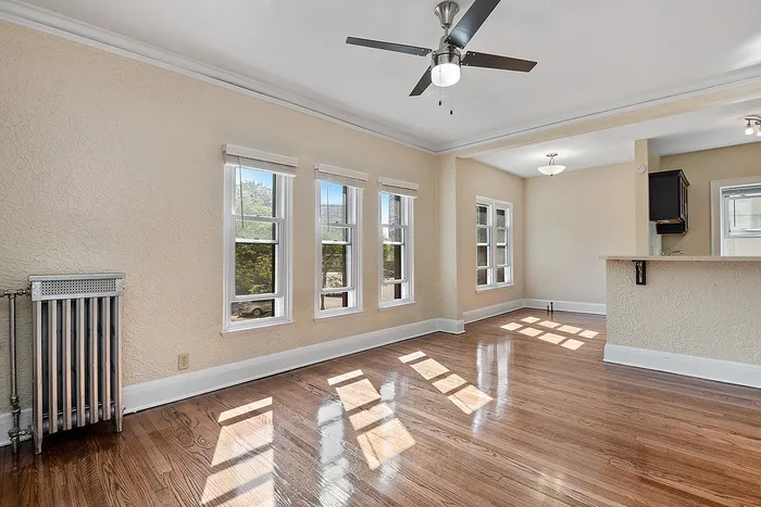 Bright and airy living space with polished hardwood floors, large windows, and an elegant ceiling fan.