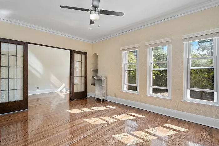 Bright and inviting living room with hardwood floors, large windows, and elegant French doors opening to a sunlit space.