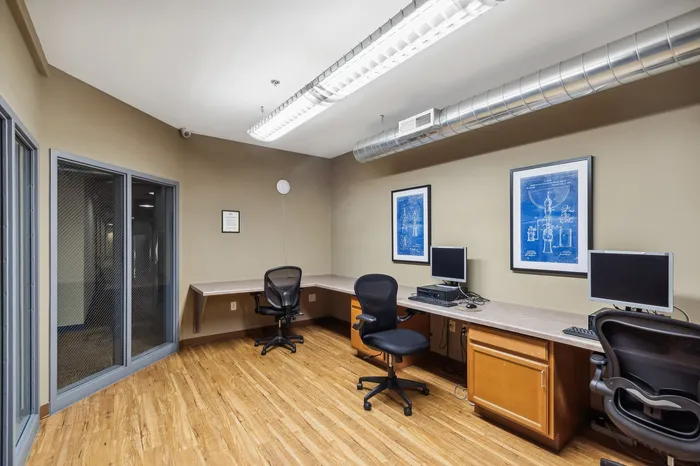 Modern and inviting office space with stylish chairs and sleek computer workstations, enhanced by warm wood flooring and elegant blueprint artwork.