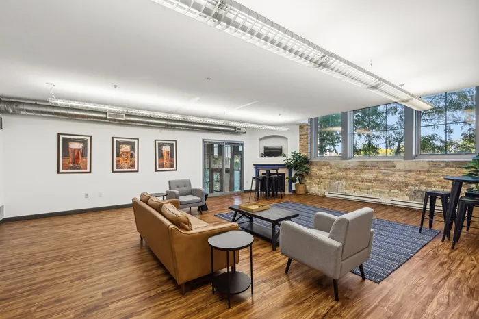 Modern, open-concept living area with stylish furniture, exposed brick wall, and large windows offering abundant natural light.