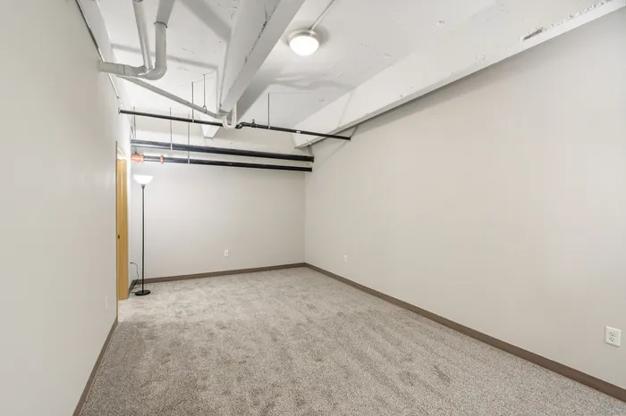Modern apartment featuring a spacious, carpeted room with stylish exposed ceiling and bright lighting.