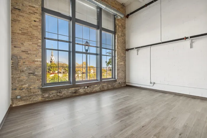 Chic loft with large industrial windows offering a panoramic cityscape view, complemented by exposed brick walls and sleek wooden flooring.