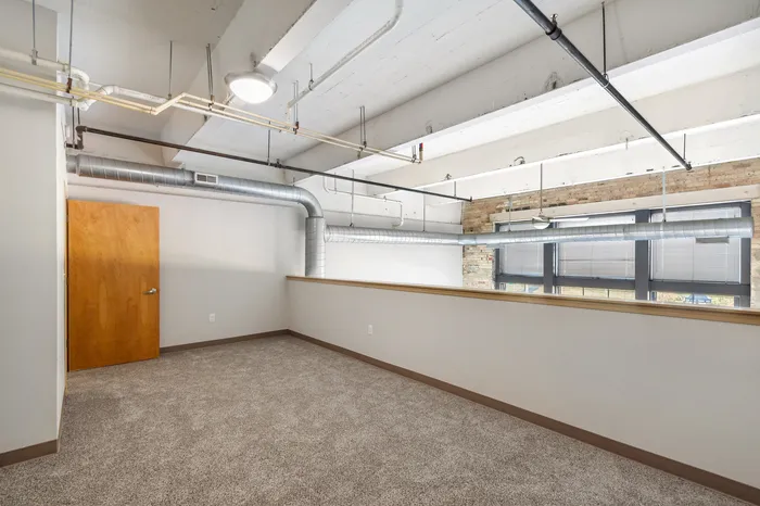 Bright and spacious loft area with exposed ductwork, carpeted flooring, and large windows, perfect for creative workspaces.