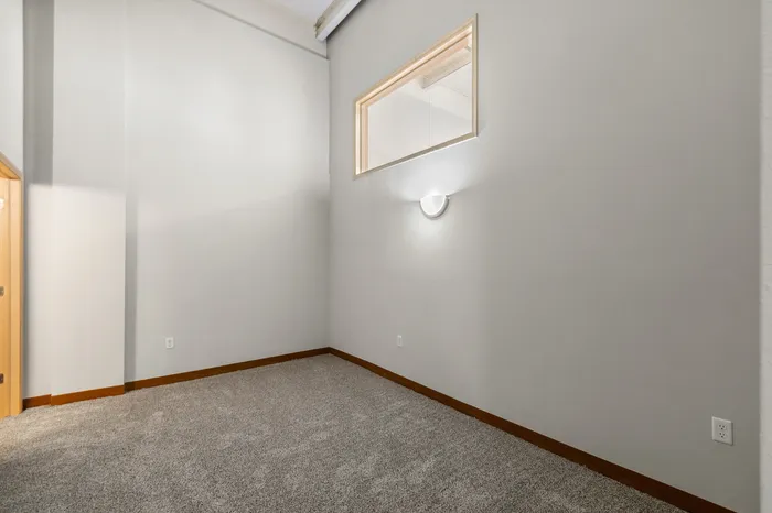 Bright, spacious room with cozy carpet, modern wall sconce, and unique internal window design.