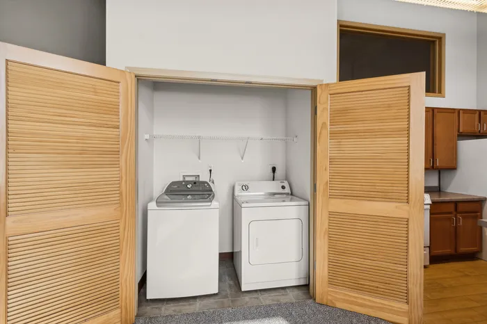 Convenient in-unit laundry with washer and dryer behind elegant wooden doors, adjacent to a modern kitchen.
