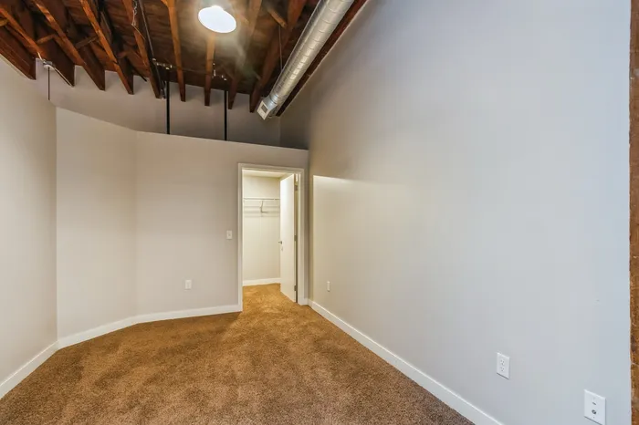 Inviting bedroom with plush carpet, exposed wooden beams, and a spacious walk-in closet, ideal for modern living.