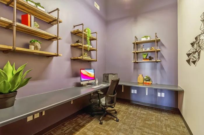 Modern home office with sleek built-in desk, stylish shelving, and potted plants against a chic purple wall.