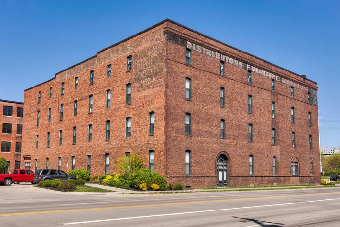 Charming historic brick building with large windows, ideal for spacious loft apartments, set against a bright blue sky.