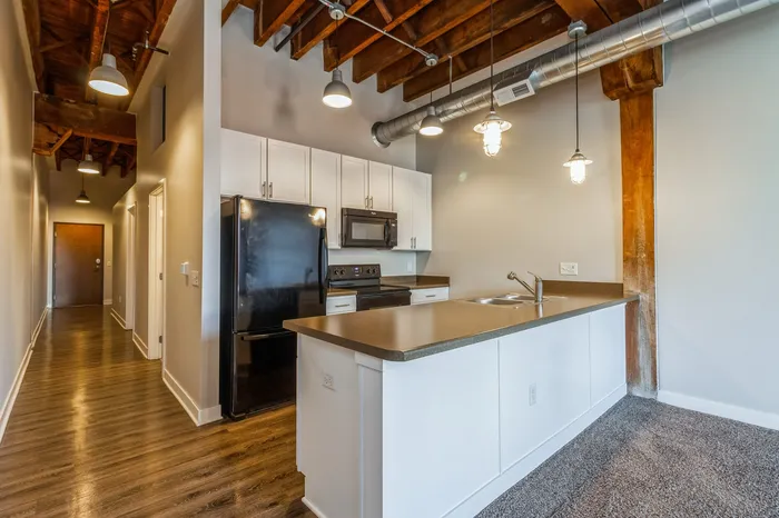 Modern kitchen with sleek black appliances, pristine white cabinets, and stylish industrial lighting under exposed wooden beams.