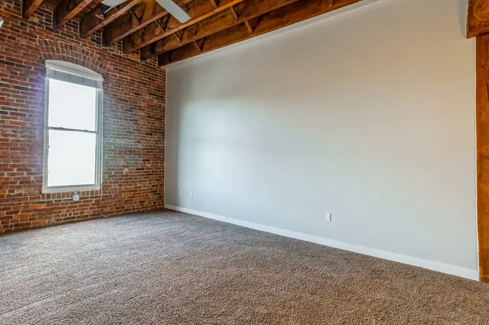 Charming loft-style room with exposed brick wall, large window, and warm wood beam ceiling, ideal for creative living.