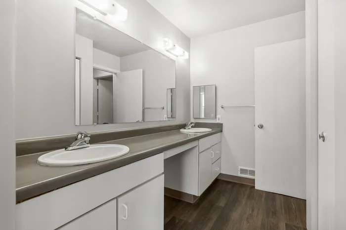 Modern bathroom with dual sinks, ample counter space, and sleek cabinetry, featuring bright lighting and elegant wood flooring.