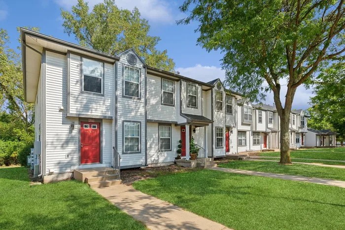 Charming townhouse row with red doors, lush landscaping, and abundant trees, offering a welcoming community vibe.