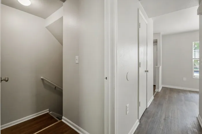 Sleek modern hallway with wooden flooring and bright natural light entering through a window, highlighting a stylish stairwell design.