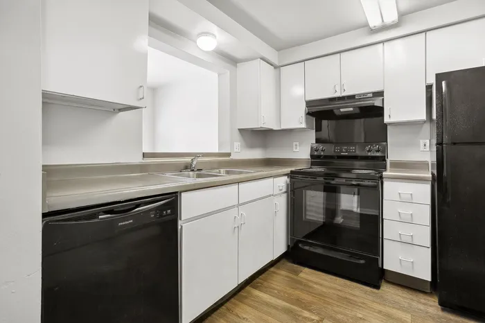 Modern kitchen with sleek black appliances, white cabinetry, and warm hardwood flooring.