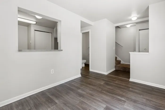 Bright, modern apartment with sleek hardwood floors, open pass-through window, and inviting carpeted staircase.