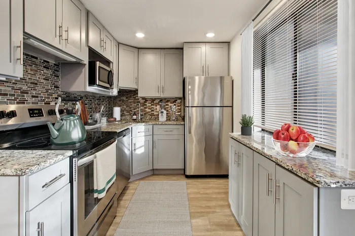 Modern kitchen with sleek stainless steel appliances, granite countertops, and stylish backsplash, featuring a large window with natural light.
