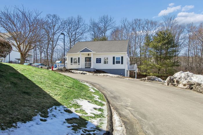 Charming single-story house with a welcoming porch, nestled in a serene, wooded neighborhood with clear blue skies.
