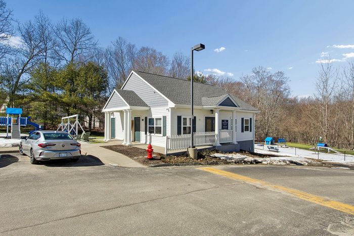 Charming single-story home with a spacious porch, surrounded by nature, featuring a modern car parked in front and a vibrant playground nearby.