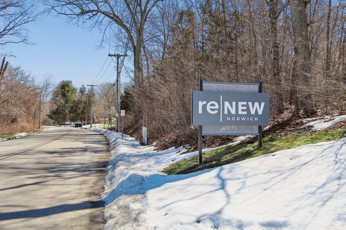 ReNew Norwich sign in a serene snowy landscape, bordered by lush woods and a quiet road.