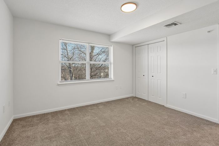 Bright and airy bedroom with plush carpeting, large window, and double closet, offering serene views of nature.