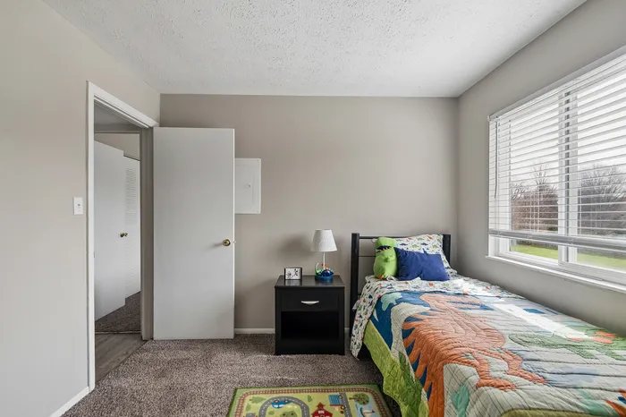 Cozy children's bedroom featuring a single bed with colorful dinosaur bedding, a plush dinosaur toy, and a window with garden views.