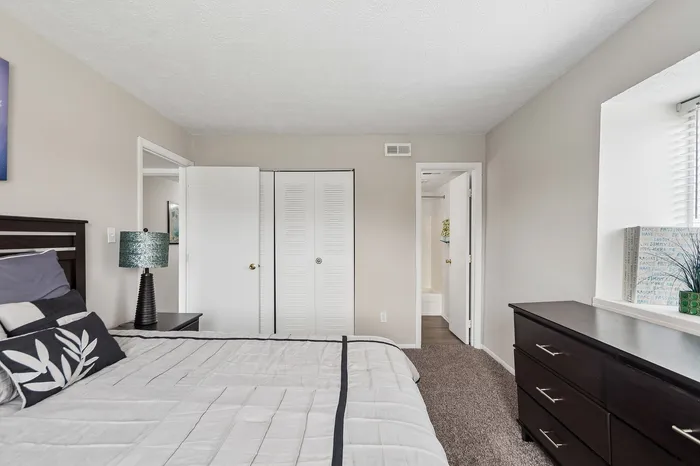 Bright and cozy bedroom with modern dresser, stylish lamp, and soft bedding, offering a relaxing retreat.